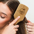 A bamboo hair brush with a logo, featuring a smooth handle and natural wood grain, being used on long hair.