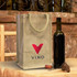 A jute wine carrier in natural colour with a red logo, alongside a dark wine bottle and cork on a rustic table.