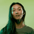 A model with long hair wears wireless earbuds against a green background. The design features a sleek, modern style.