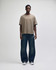 A unisex boxy T-shirt in a shade of brown, worn with loose-fitting blue jeans. The model stands upright against a plain background.