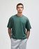 A green heavyweight cotton unisex boxy t-shirt, worn by a model with short hair, paired with grey sweatpants.