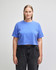A blue, heavyweight cotton women's crop boxy T-shirt displayed on a model, featuring a logo.