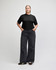A black mid-length boxy top paired with light blue trousers, worn by a model standing upright. The outfit features a casual style.