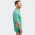 A man in a green polo shirt stands smiling, with a logo on the shirt's chest.