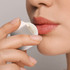 A Cube Lip Balm being applied to lips, held delicately between fingers.