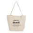A cream tote bag with a logo featuring the text "Coastal Breakers Surf Club" and a date.