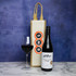 A jute single wine bag in cream with a brown handle, alongside a bottle of red wine and a glass filled with wine.