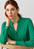 A green long sleeve blouse with a V-neck design, featuring button details on the sleeves. The model poses thoughtfully.
