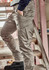 A model wearing beige cargo pants, featuring multiple pockets, standing on a wooden staircase.