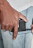 A close-up of a hand placing a phone into the pocket of light blue stretch jeans. The jeans feature a subtle logo.