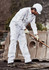 A man in white work pants is using a tool on a construction site, wearing a helmet and gloves.