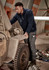 A man in a navy 1/4 zip polar fleece works on an engine in a workshop, wearing work pants with pockets.