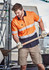 A short sleeve work shirt in orange and navy with reflective tape, worn by a man using a shovel, with a construction setting in the background.