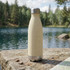 A drink bottle in a light beige colour with a stainless steel base, set against a scenic lakeside background.