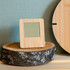 A bamboo desk clock with a square face, set on a rustic wooden surface against a textured wall.