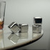 A set of shiny silver whiskey ice cubes resting on a smooth surface, beside a glass of drink.