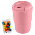 A reusable pink coffee cup with a textured grip, accompanied by a pack of colourful jelly beans.