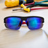 Sporty black sunglasses with blue reflective lenses, positioned on a wooden surface near tools. Features a logo.