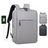 A grey backpack with a front pocket, featuring a USB charging port and black straps, with a logo on the side.