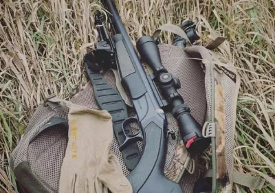 Gun with scope on backpack in grass field.