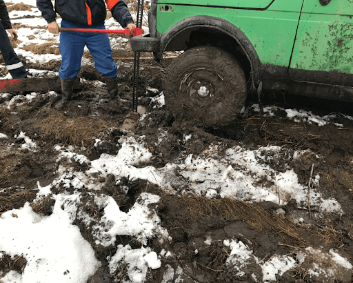 Off-road hi-lift jack in use on a green vehicle stuck in mud and snow