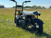 TrailMaster Storm 200 MiniBike, front view of a black mini bike with thick tires and a plastic cover on the seat, outdoors on a grassy field.