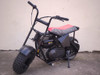 TrailMaster Storm 200 MiniBike, compact black mini electric dirt bike with chunky tires and a red seat.