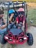 Assembled TrailMaster Mini XRX/R+ Go Kart with Reverse for Ages 4+, red, with two children wearing helmets sitting inside, on grass outdoors with a man nearby.