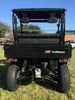 Trailmaster Taurus 200U Utility SXS UTV, front view showing rugged tires, suspension system, and open cargo bed on a grassy field with a clear blue sky.