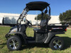 Trailmaster Taurus 200U Utility SXS UTV, black compact utility vehicle with sturdy tires, roof, and cargo bed, parked on grass with clear blue sky.
