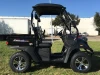 Trailmaster Taurus 200U Utility SXS UTV, black compact off-road vehicle with four wheels, black roof, and side mirrors, parked on grass in outdoor setting.
