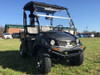 Trailmaster Taurus 200U Utility SXS UTV, black color off-road vehicle with a canopy and large tires, parked on grass field during daytime.