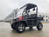 Trailmaster Taurus 200U utility SXS UTV, black and red off-road vehicle with rugged tires and a canopy, parked on an open paved area outside a modern building.