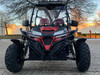 TrailMaster Cheetah 300EX Deluxe EFI Go-Kart/UTV Crossover, front view of a rugged off-road vehicle with black and red body design, large off-road tires, protective bars, and LED light bar on the roof, set against an outdoor background at sunset.