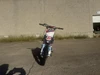 TrailMaster SK110S 110cc Semi-Automatic Kids Dirt Bike, front view of the small dirt bike in an outdoor setting with a beige wall and garage door in the background.