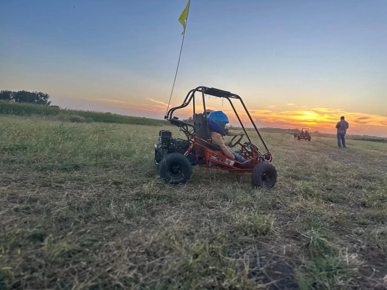 TrailMaster Mini XRX/R+ Go Kart with Reverse, assembled on a grassy field during sunset, with a child wearing a helmet driving and an adult standing in the background.