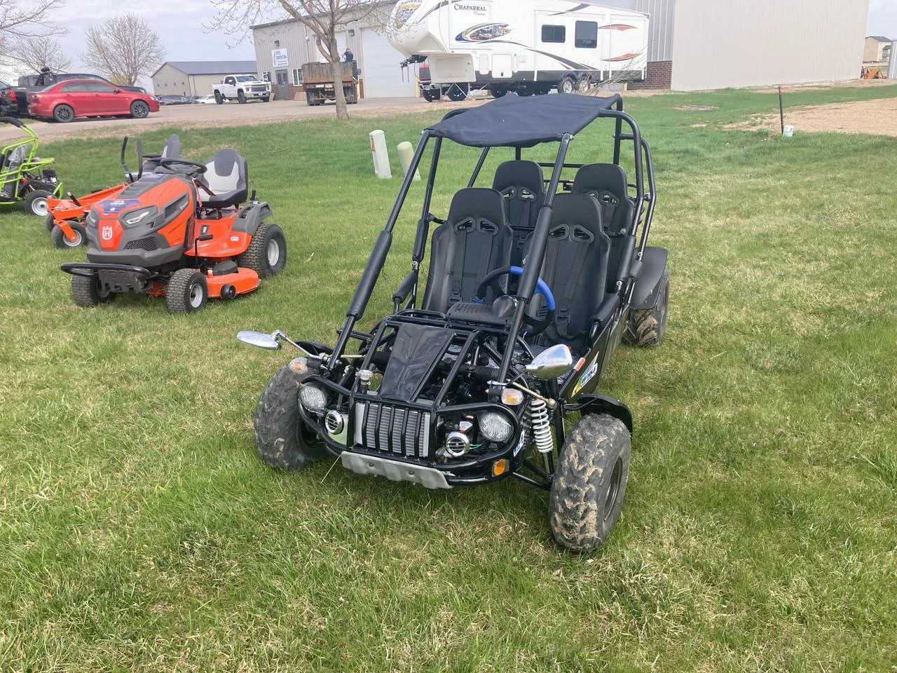 TM 300 XRS-4E 4 Seater Go Kart for Families, outdoor scene on grassy field with other small vehicles and machinery in the background.