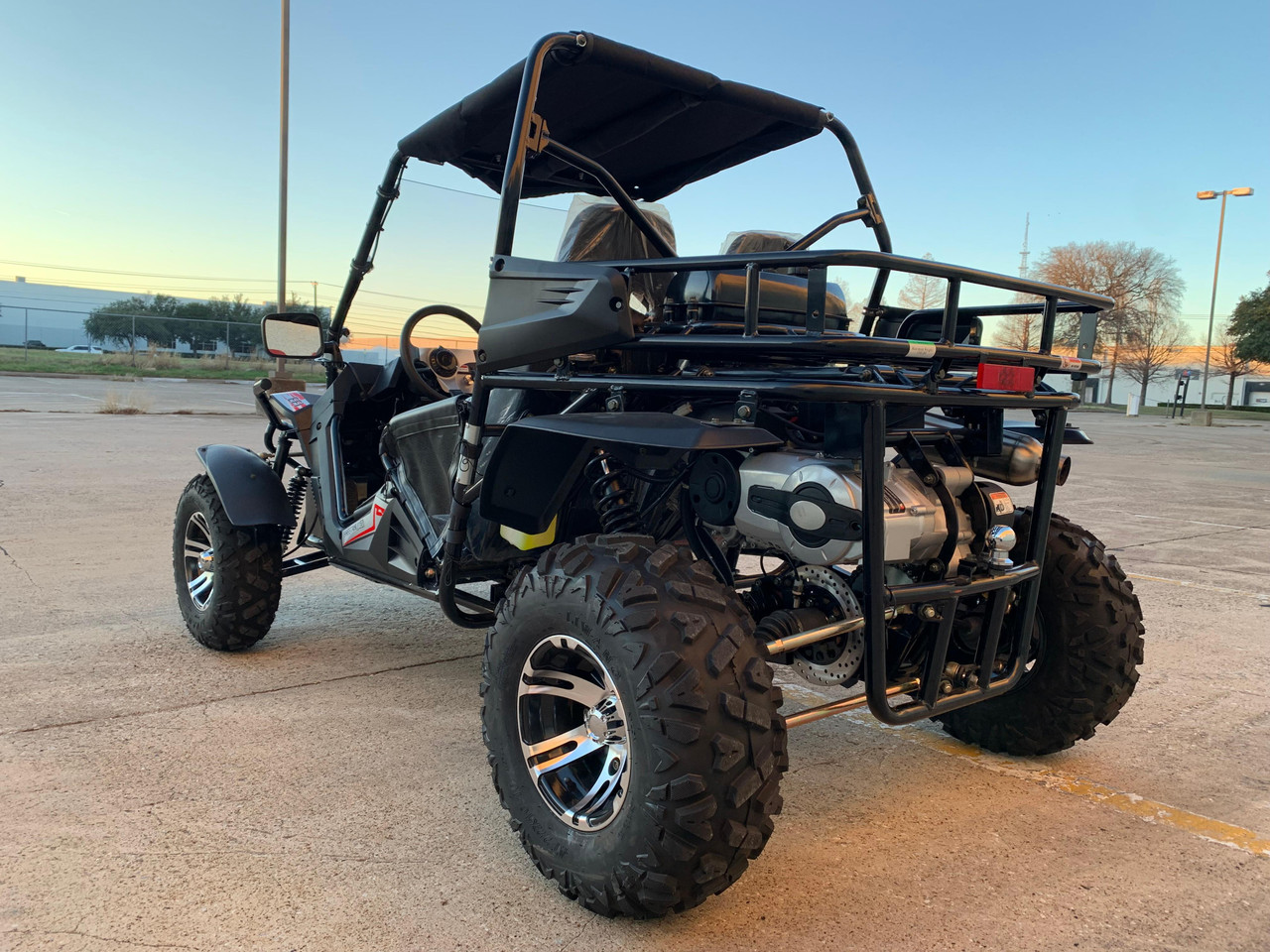 TrailMaster Cheetah 300EX Deluxe EFI Go-Kart/UTV Crossover, rugged off-road vehicle with large tires and protective frame in an outdoor parking lot at sunset.