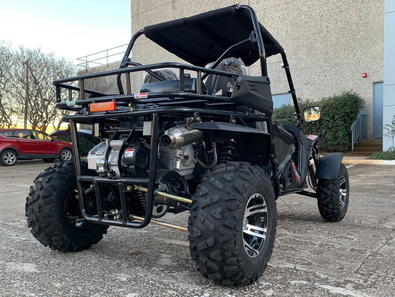 TrailMaster Cheetah 300EX Deluxe EFI Go-Kart/UTV Crossover, rugged off-road vehicle with large tires, black frame, and roof canopy in an outdoor parking lot.