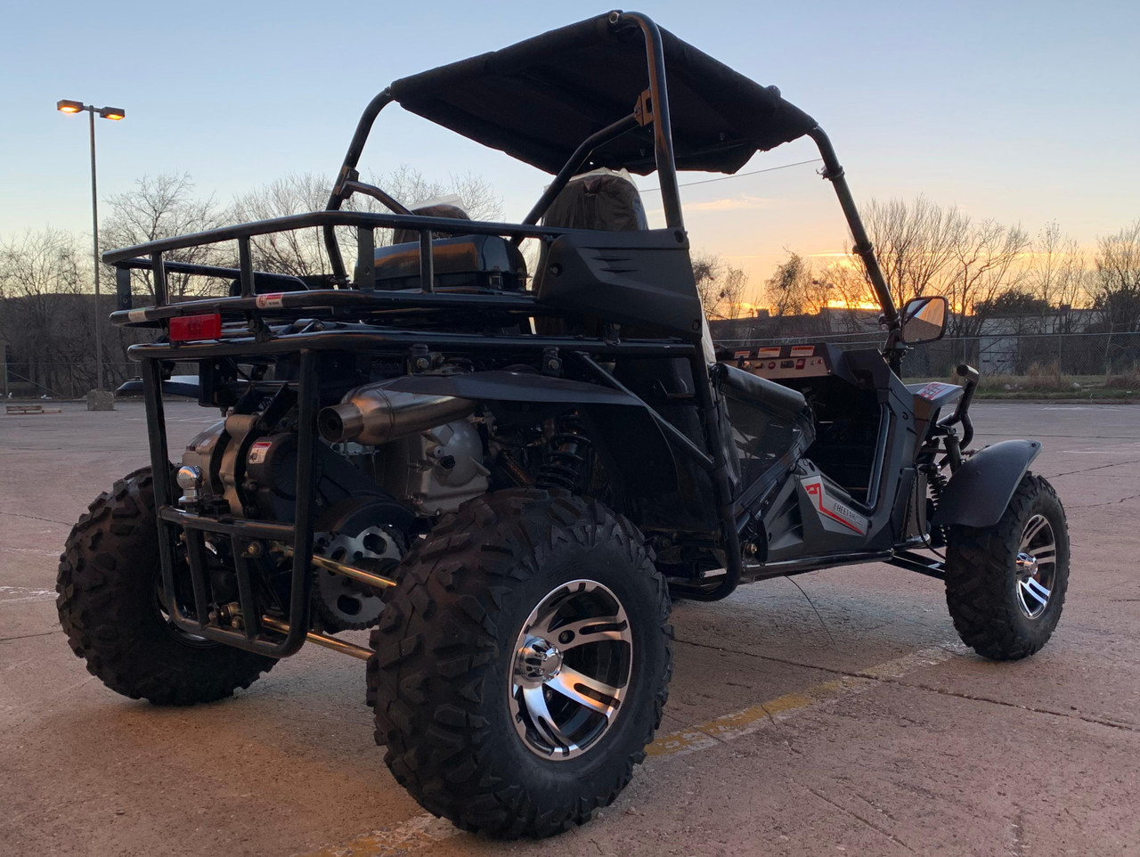 TrailMaster Cheetah 300EX Deluxe EFI Go-Kart/UTV Crossover, black off-road vehicle with rugged tires, racing seat, and protective roll cage parked on a paved lot at sunset.