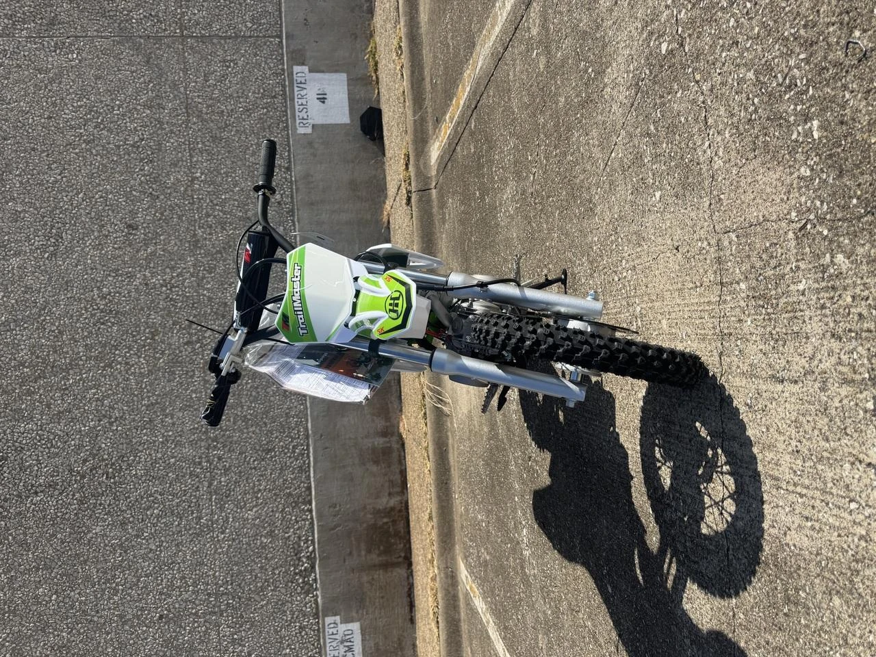 TrailMaster SK110A 110cc Fully Automatic Kids Dirt Bike, front view showing green and white color with black tires on asphalt ground.