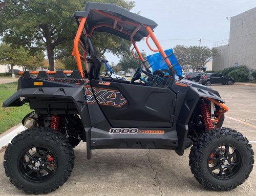 TrailMaster 4x4 SportsCross 1000 Side by Side, black and orange off-road utility vehicle with rugged tires, suspension system, and side-by-side seating in an outdoor parking lot.