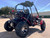 TMBlazer 200EX PREMIUM Sport Go Kart, a rugged off-road go-kart with large tires and a protective roll cage, parked outdoors under a clear blue sky.
