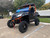 TM 4x4 SportsCross 1000 Side by Side, rugged off-road vehicle with black body, orange roll cage, large knobby tires, and blue windshield, parked in an outdoor lot.