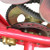 TM Mid XRX Go Kart for age 8 and up, close-up of the engine and chain drive system with metallic and black components.