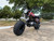 TM Hurricane 200X Upgraded Mini Bike, rugged off-road motorcycle with large knobby tires and a red and black color scheme, parked on a concrete surface under a tree.