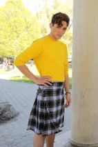 Young man in black, white and lilac tartan kilt with yellow sweater by a column