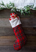 Christmas stocking in red tartan with white cuff filled with gifts, hanging on a wooden wall