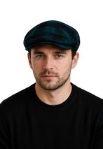 Button down plaid flat cap in dark green and navy tartan worn by a man, front view