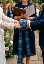 Couple's hands bound with a blue and green tartan handfasting ribbon at an outdoor wedding